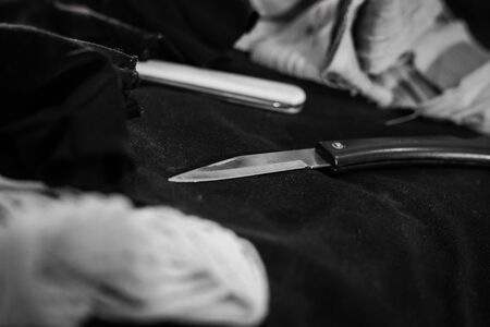 pocket knife with some bandage are on the black cloth under red light. Close up -  B/W
