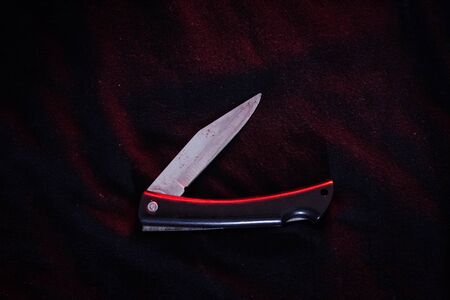 a pocket knife on the black cloth under red light. nearly keep in pocket.の写真素材