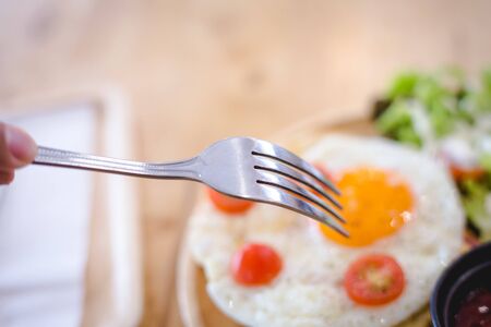 fork preparing to hit fried egg on Sandwich ham cheese serve with wooden plate