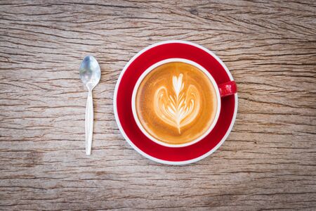 coffee with milk making for flower picture in red cup on plate and spoon put on bark wooden tableの写真素材