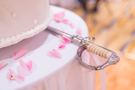 closeup wedding sword for cake put near wedding cake in soft pink tone decorate with flower and some petalの写真素材