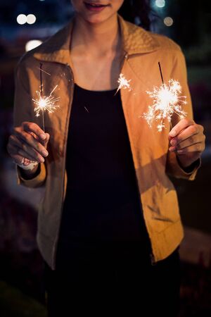 lady hold two firesparklers blink in her hand at night toning, with smile faceの写真素材
