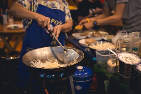 Woman cooking put onion slice into pan with people are eating in backgroundの写真素材