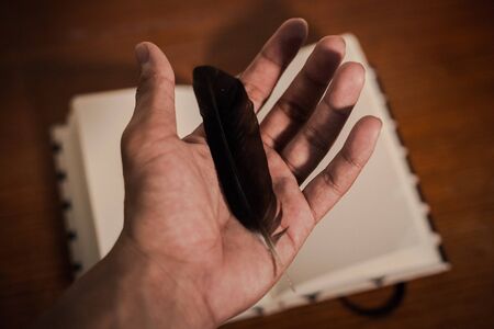 feather on hand with lecture note book opening show empty page on wood table in backgroundの写真素材