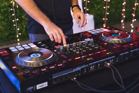 DJ is mixing some music with controller at outdoor night party, by moving hand to set many buttonの写真素材