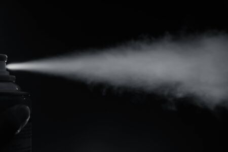 Smoke spray spit from bottle on left side with finger pressing on black background.