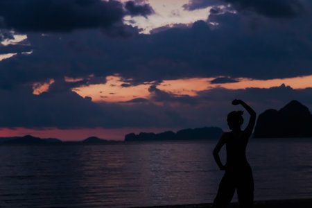 Lady in silhouette do yoga with Twilight sky colorful and cloudy over the beach on backgroundの写真素材