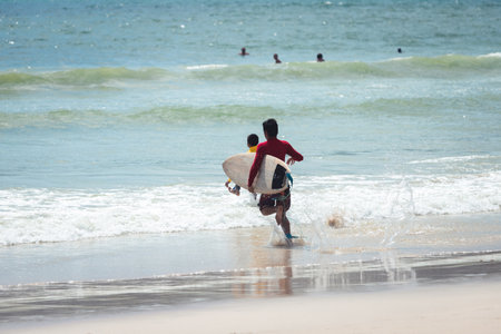 Thai guys running with surfboard in a hand to the sea to play surf in sunny day with some wave...