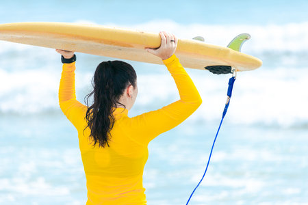Girl holding surfboard put on her head waiting for wave in front of the beach in sunny dayの写真素材