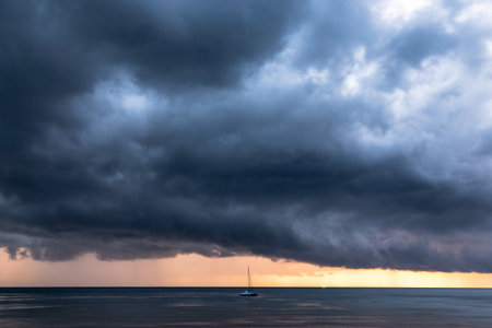 Storm coming lead scary cloud in dark mode with strong wind on the sky over the ocean, one yacht boat alone on the seaの写真素材