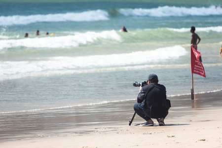 Photographer guy sit and wait to taking photo something on the sea with telescope zoom len on pro camera with tripod, have red flag in Thai language for cautionの写真素材