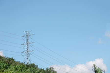 Big electric pole with power line in pattern against soft blue sky and some cloud put in the forest