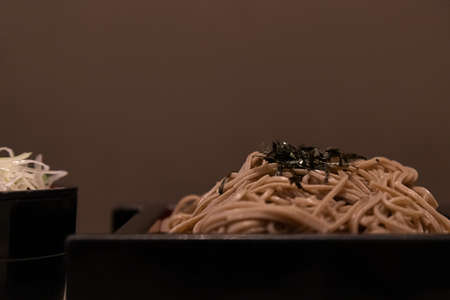 Cold noodle in japanese style with sauce soup in a small bowl on brown background