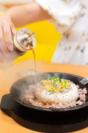 meat with rice have vegetable on top put on hot plate after cook make steam flow over, putting sauce into itの写真素材