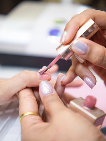 A close-up view of a manicure session showcasing an elegant nail polish application in soft pink. The delicate technique emphasizes beauty and self-care.の写真素材