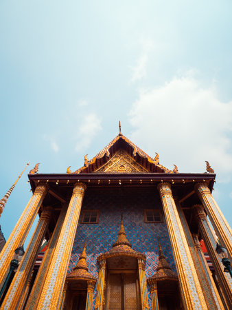 A stunning view of a Thai temple showcasing its intricate golden architecture against a clear blue sky, highlighting cultural beauty and artistic details.の写真素材