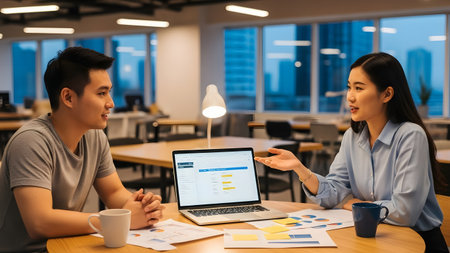 Two professionals engage in a discussion around a laptop in a modern office. The atmosphere is collaborative, showcasing teamwork and strategy in a bright workplace.の素材