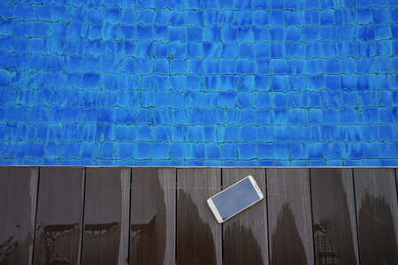 Mobile phone on wooden deck near swimming poolの写真素材
