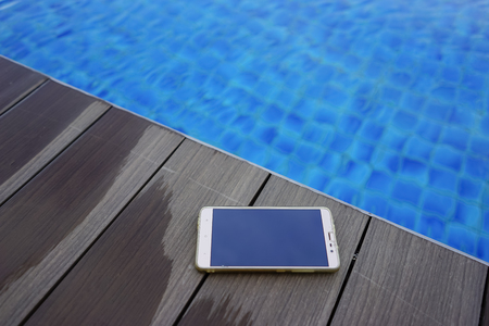 Mobile phone on wooden deck near swimming poolの写真素材