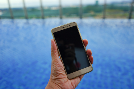 Hand holding mobile phone on swimming pool background. Closeup copy space photoの写真素材