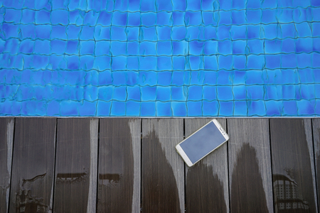 Mobile phone on wooden deck near swimming poolの写真素材