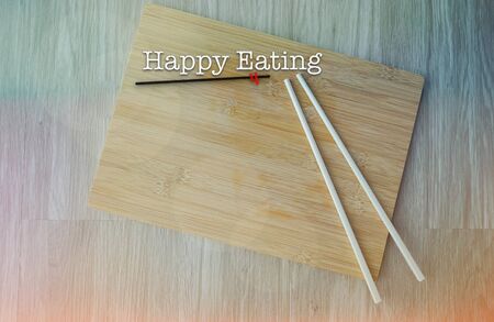 Chopsticks and chopping board on wooden table with word HAPPY EATINGの写真素材