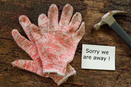 Working gloves and hammer on wooden table with words Sorry We Are Away written on a piece of paperの写真素材