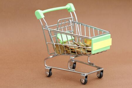 Trolley filled with coins on brown background. Concept of spending,purchasing,financialの写真素材