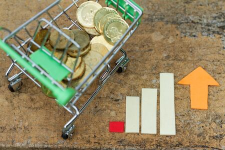 Trolley filled with coins beside chart showing increasing / rising trend. Concept of growth in...