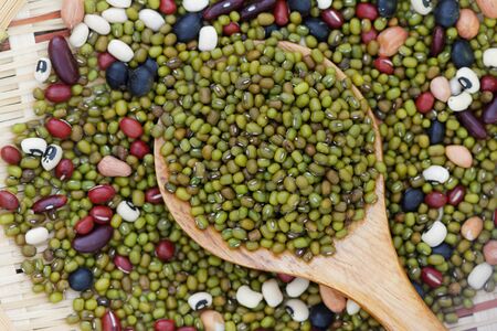 Mung beans in wooden spoon with mixed beans in rattan tray in the backgroundの写真素材
