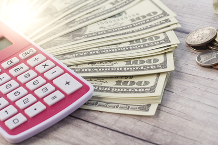 100 US dollar and coins with calculator on wooden background with soft light at the corner of image. Conceptualの写真素材
