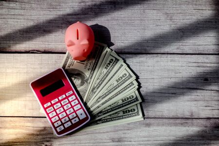 US dollar with piggy bank and calculator on wooden background with stripes of shadow with soft light at the corner. Concept of financial trap,debt and crisis and hope.の写真素材