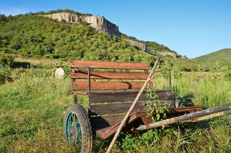 deserted cart on grass against mountainの写真素材