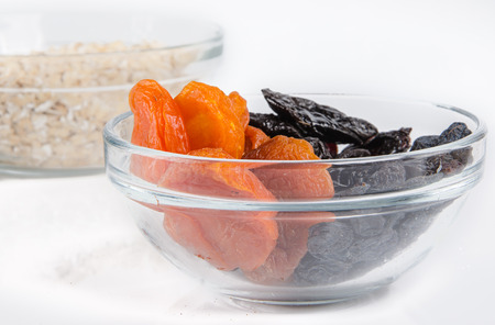 oatmeal in a glass bowl and dried fruits on white backgroundの写真素材