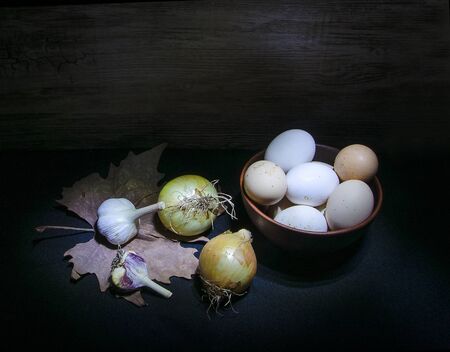 eggs in ceramic bowl and vegetables in darkの写真素材