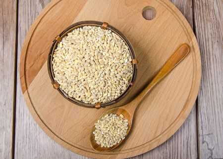 pearl barley in wooden bowl with wooden spoon on old plank tableの写真素材