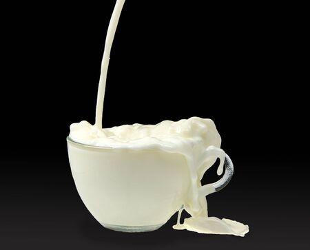 overflowing cup with milk in darkの写真素材