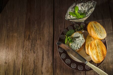 Slices of French baguette with green cream cheese and herbs on a wooden table in the darkの写真素材