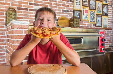 joyful teenager and pizza in his hand in cafeの写真素材