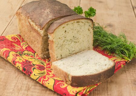 White bread loaf with dill on red tablecloth on wooden table