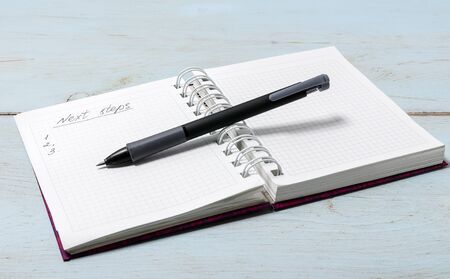Open notebook on wooden table with pencil. The inscription in the notebook "Next steps"の写真素材