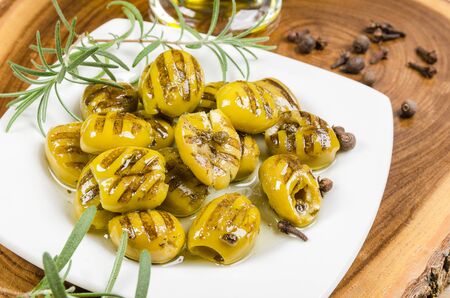 grilled green olives on plate with rosemary and spice on wooden slabの写真素材
