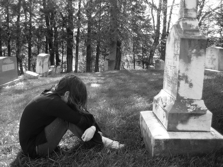 A grieving girl mourns in a graveyard, curled up in front of a large grave.の写真素材