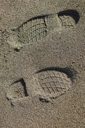 Closeup of boot footprints in soft sand on the beach.