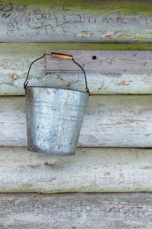 Old retro bucket hanging on wooden shelter wall.の写真素材