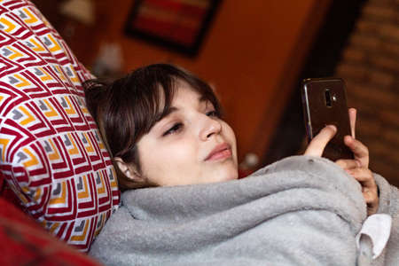 Happy beautiful girl using smart phone on the sofa
