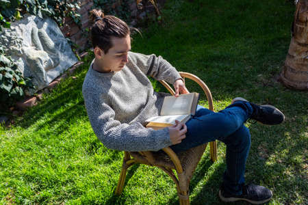 Young boy reading sitting on a chair in his garden