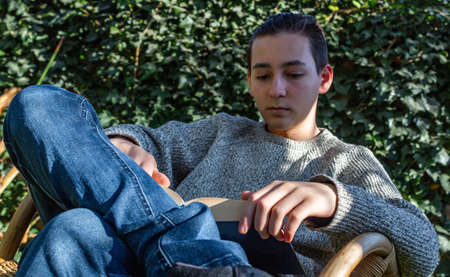 Young boy reading sitting on a chair in his gardenの写真素材