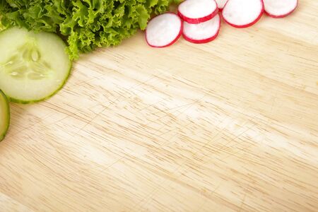 Wooden board with cucumber, lettuce and radishの写真素材