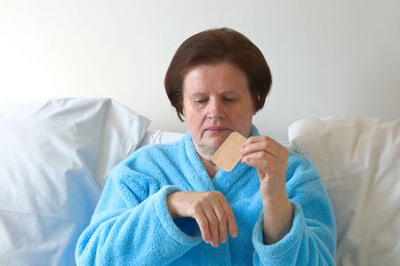 Senior woman in bed applying a plaster on her hand.の写真素材